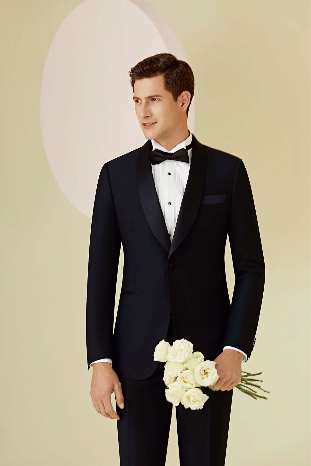 A man in a tuxedo is holding a bouquet of white flowers.