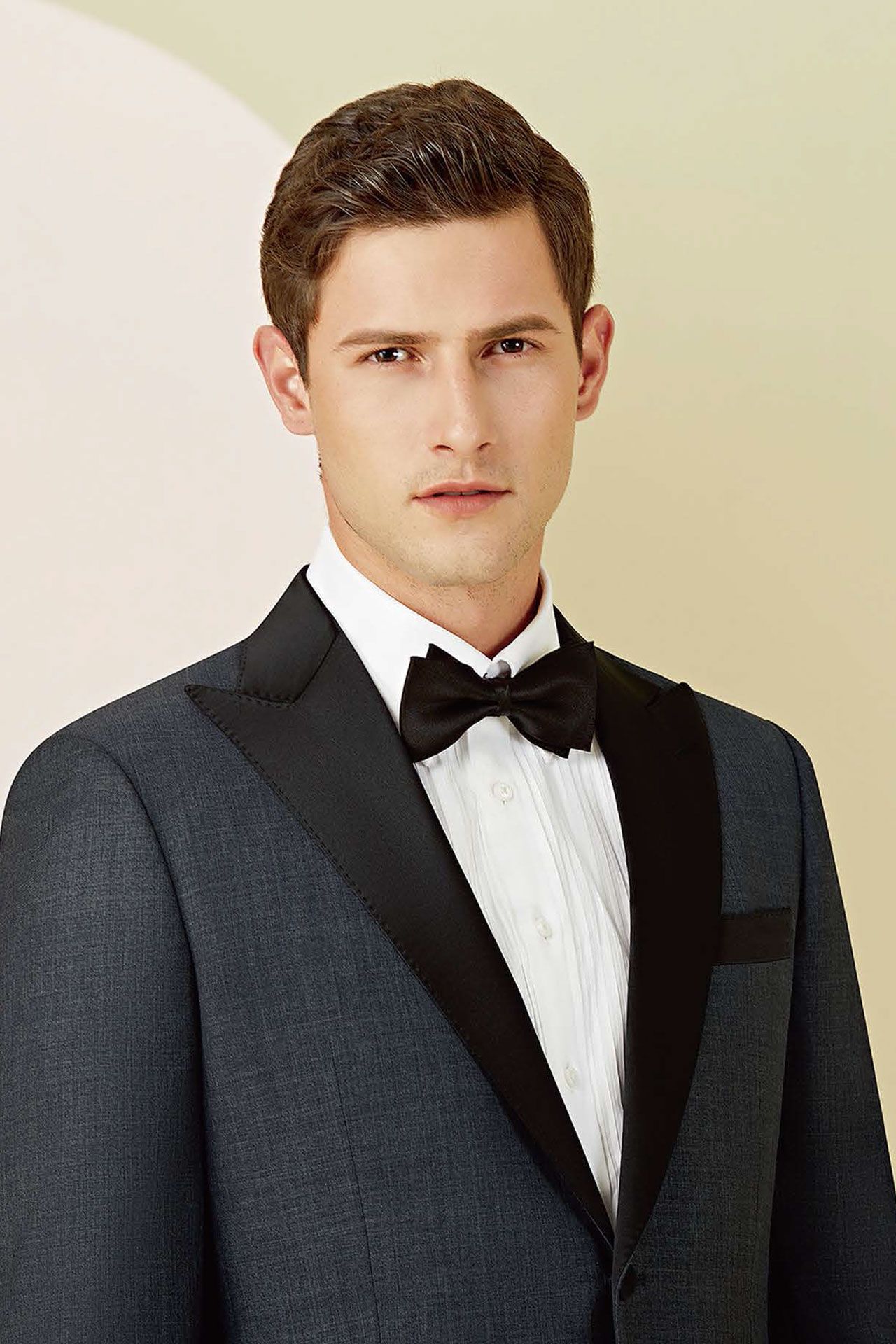 A man in a tuxedo and bow tie is standing in front of a wall