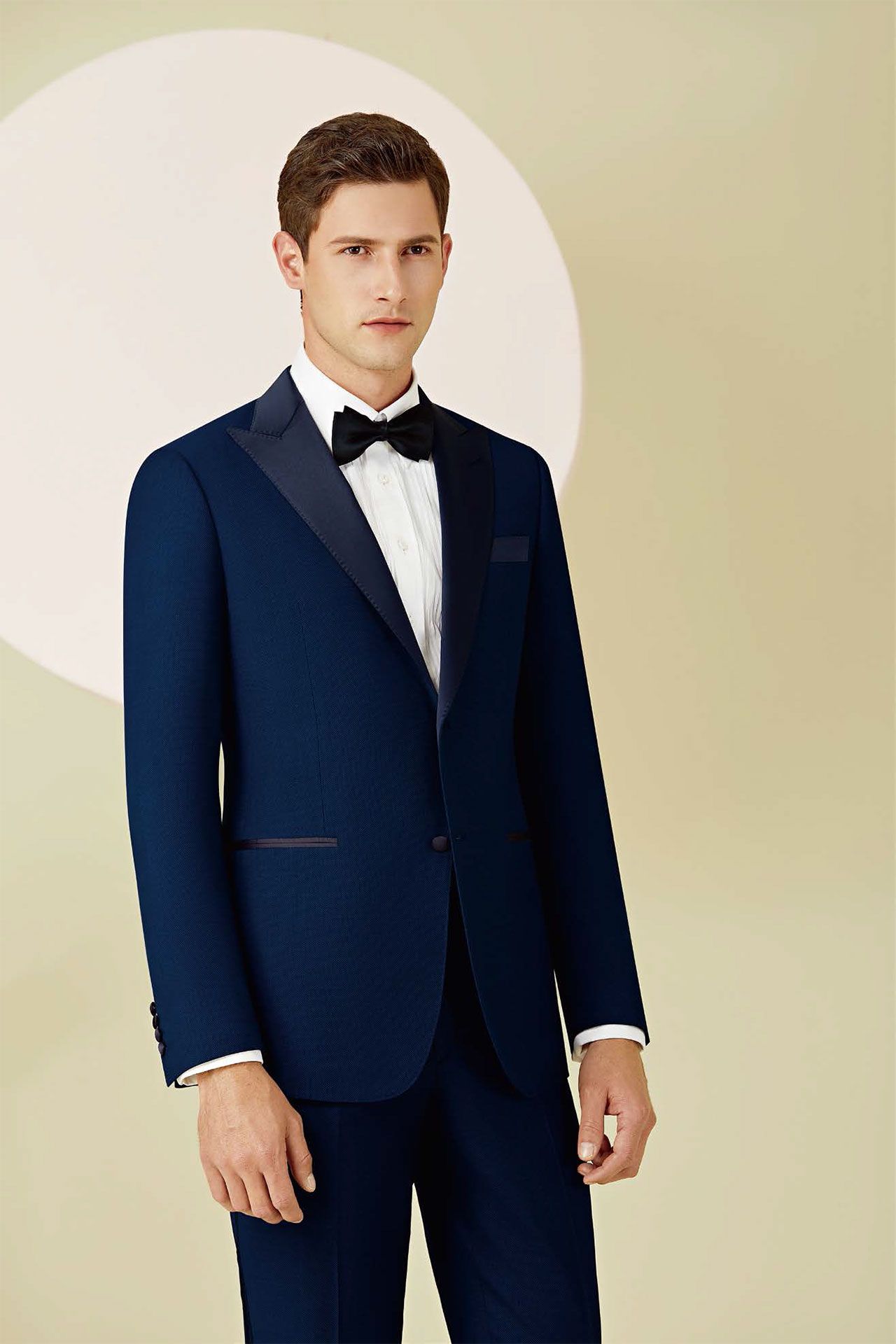 A man in a tuxedo and bow tie is standing in front of a circle.