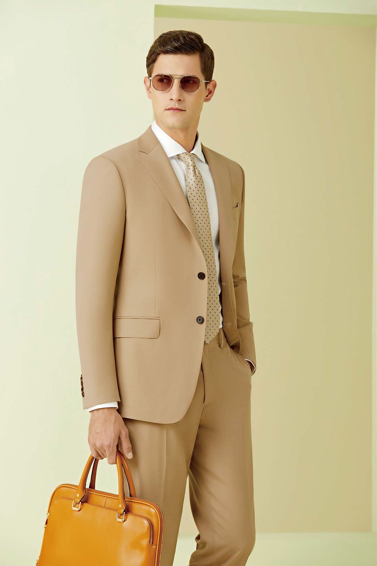 A man in a tan suit and tie is holding a brown briefcase