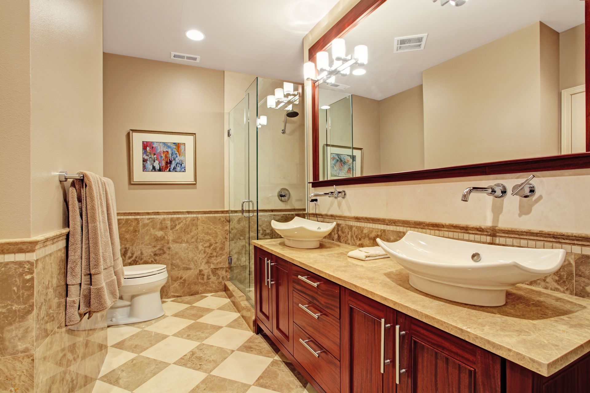 Bathroom with brown vanity, two vessel sinks, large mirror, and beige tile floor.