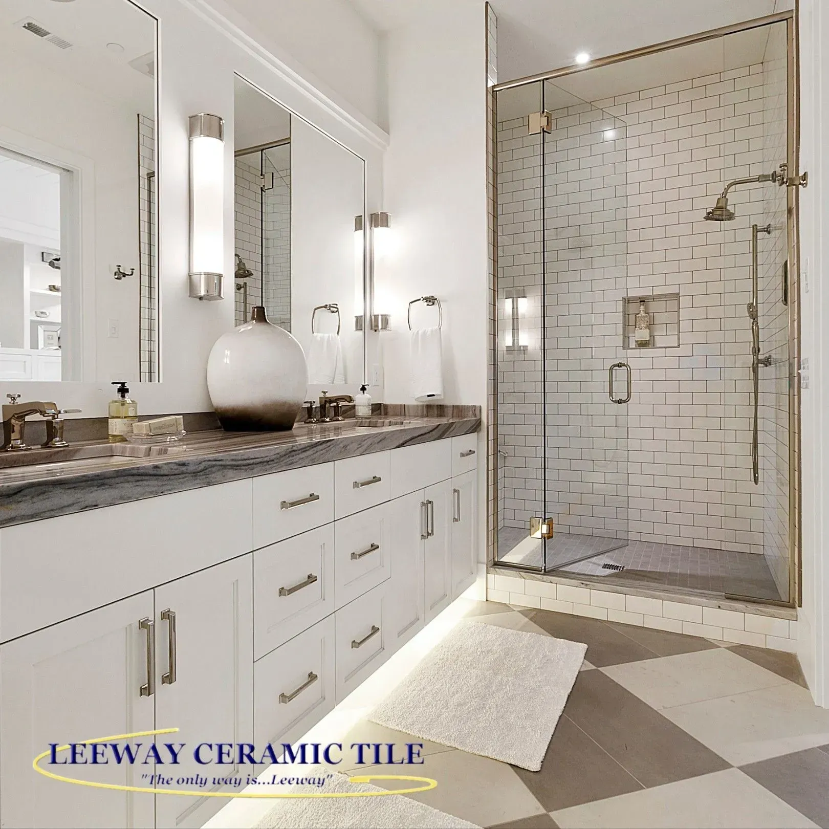 Bathroom with white cabinets, marble countertop, and a glass shower. Floor has gray and white tiles.