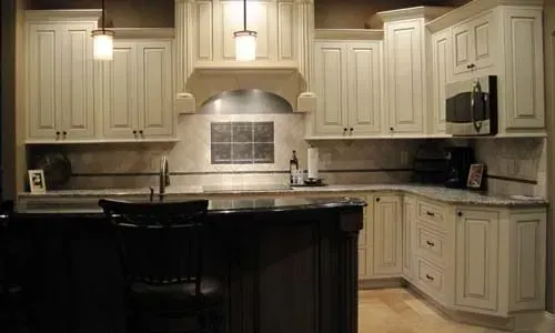 Cream-colored kitchen cabinets and granite countertops. Island with dark cabinets, stool, and pendant lights.