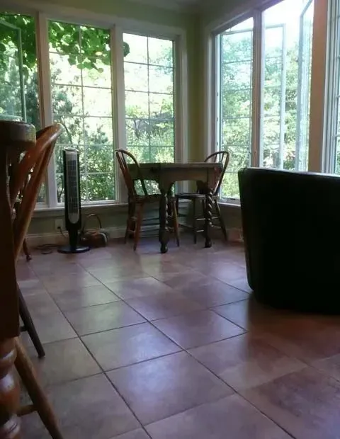 Sunroom with tile floor, table and chairs, large windows overlooking greenery.