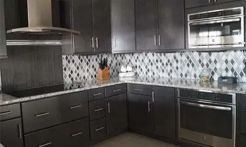 Dark gray kitchen with stainless steel appliances, mosaic tile backsplash, and granite countertops.