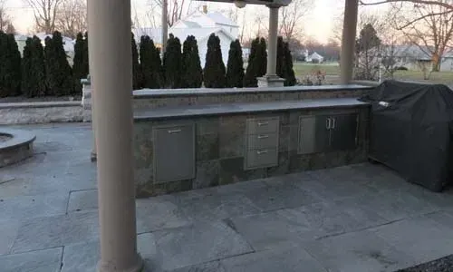 Outdoor kitchen with stone counters, stainless steel cabinets, and a covered grill.