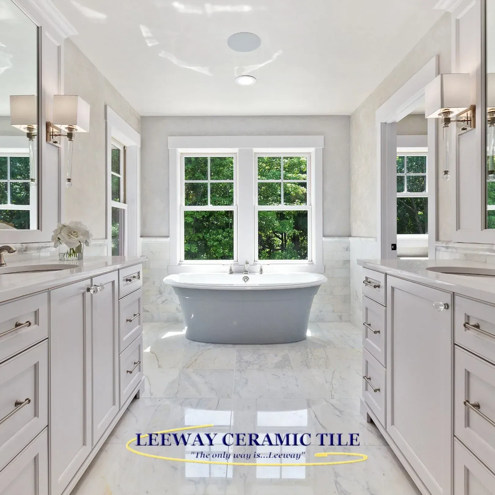 Elegant white bathroom with gray bathtub, bright windows, marble tile floor, and double sinks.