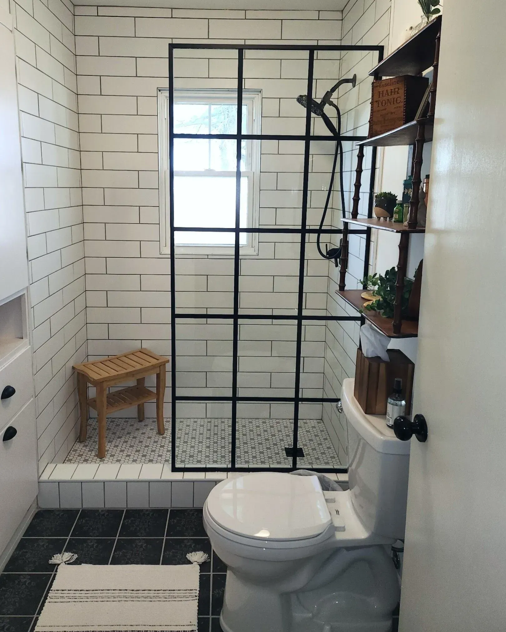 Bathroom with subway tile, black shower frame, toilet, small wooden bench, and shelves.