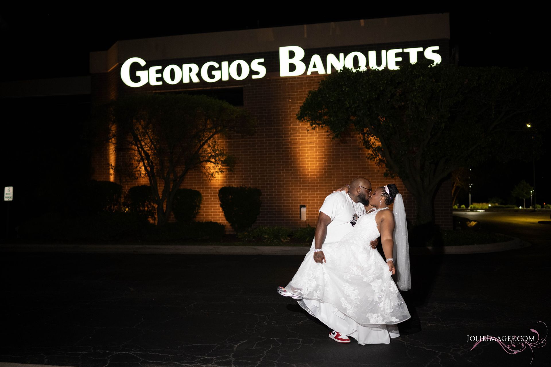 A bride and groom are kissing in front of georgios banquets