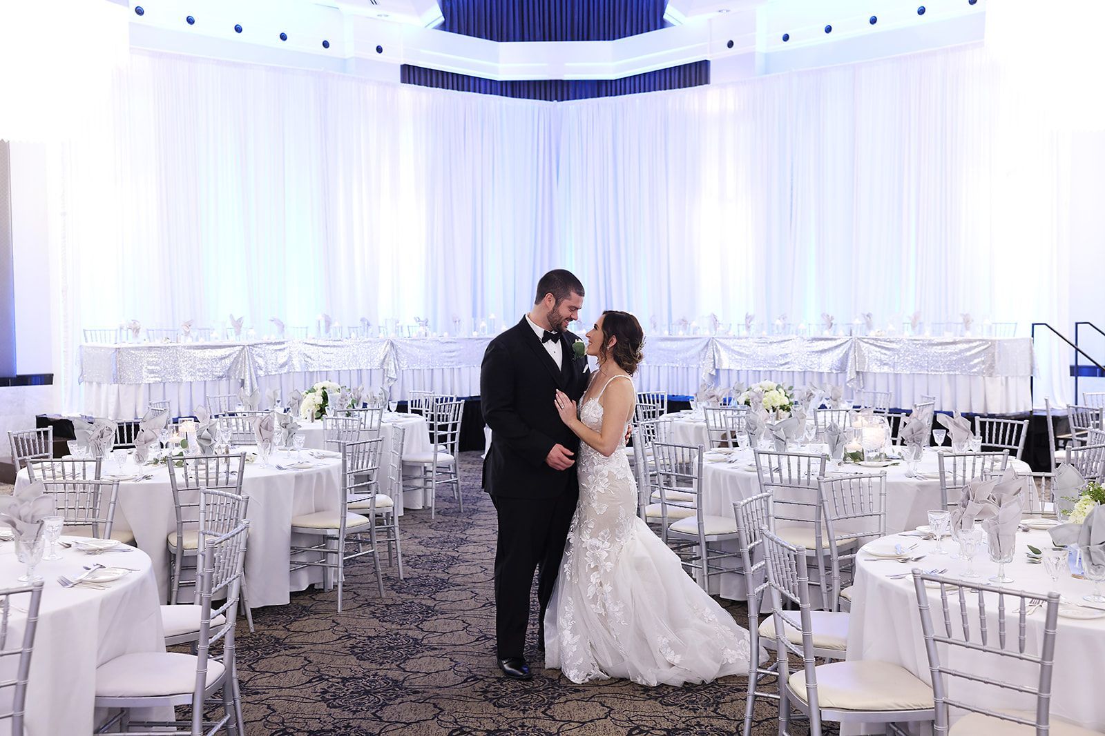 A bride and groom are kissing in a ballroom filled with tables and chairs.