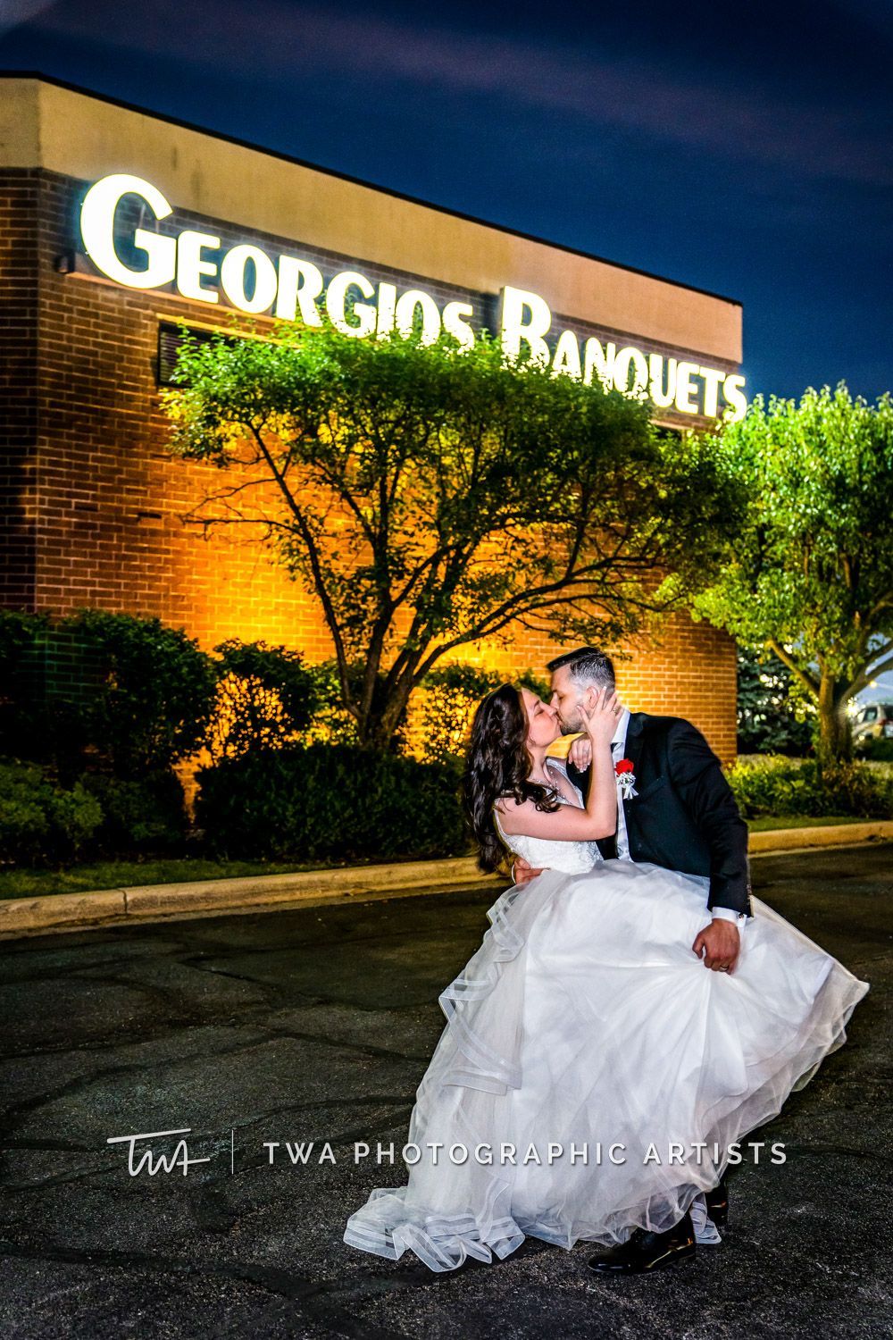 A bride and groom are kissing in front of a building.