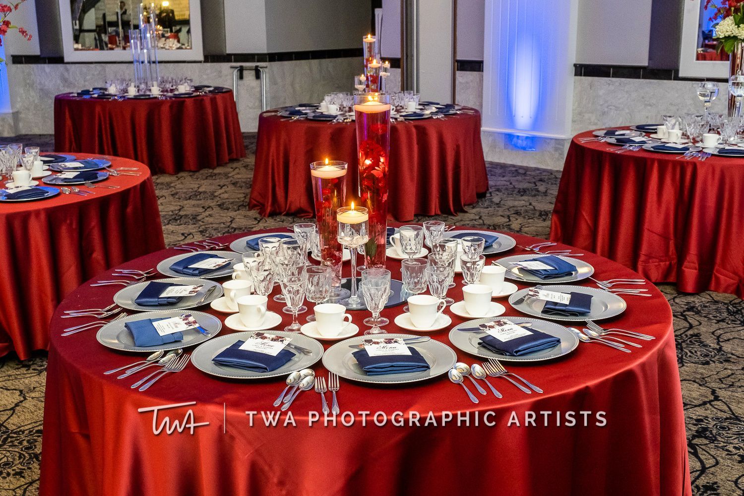 A table set for a wedding reception with a red table cloth