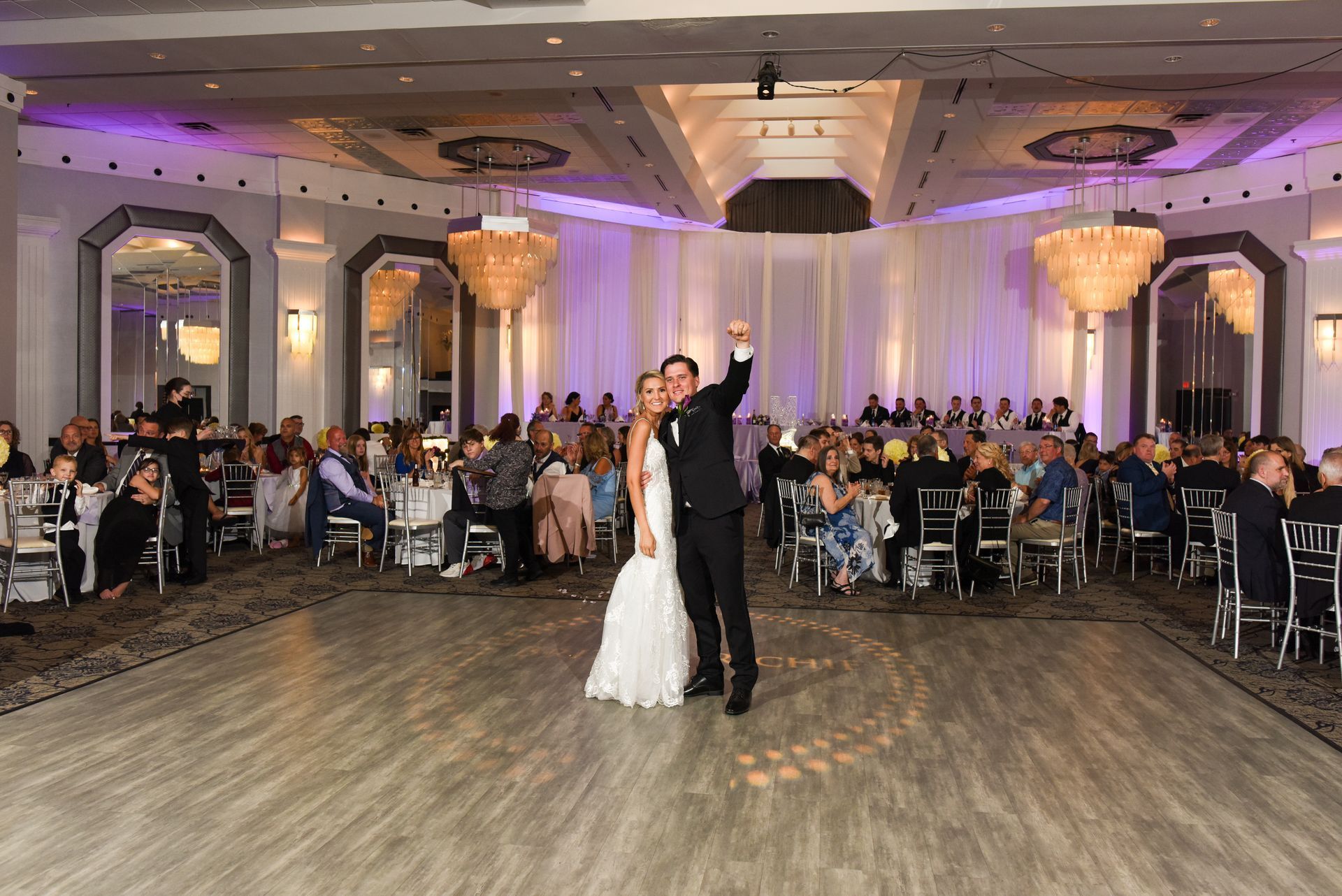 A bride and groom are dancing in a large ballroom at their wedding reception.