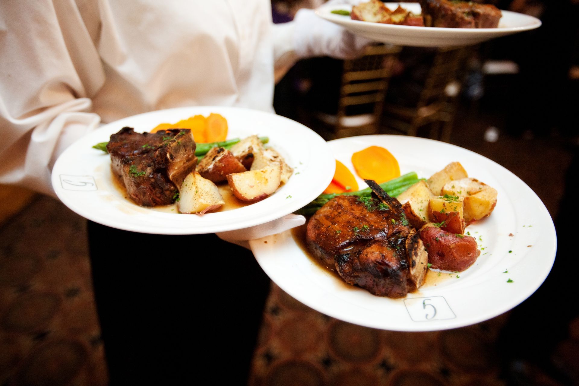 A waiter is carrying two plates of food including meat and potatoes
