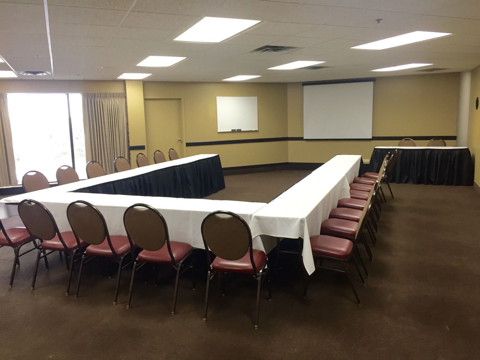 A conference room with tables and chairs and a projector screen