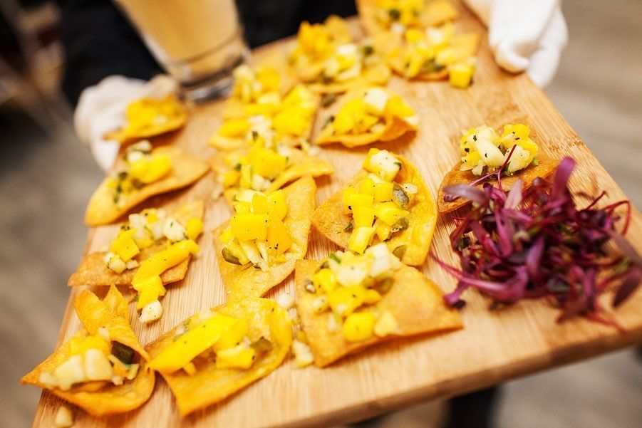 A server holds a wooden tray of mango salsa appetizers and shredded red cabbage.