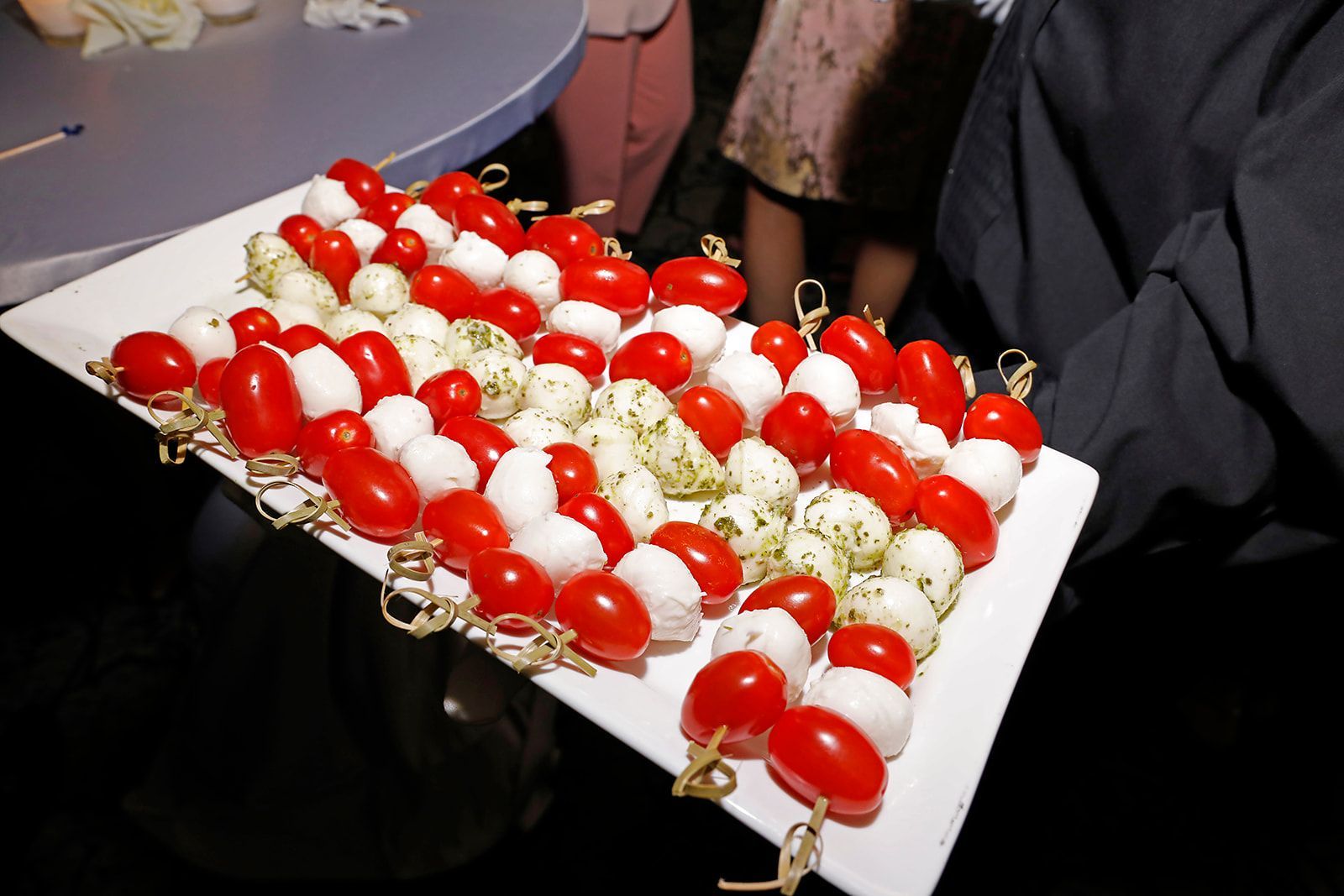 Person holding a tray of tomato and mozzarella skewers, a party appetizer.