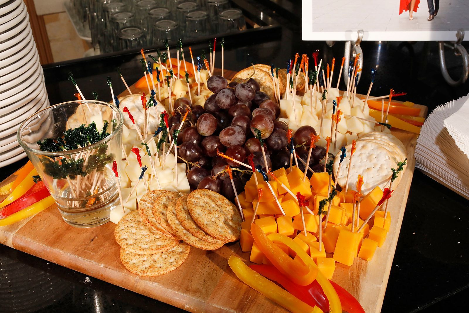 Charcuterie board with grapes, cheese cubes, crackers, and peppers on a wooden board.