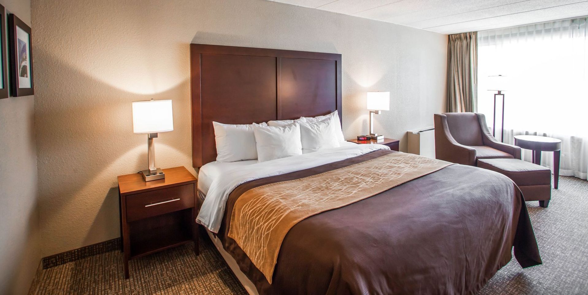 Hotel room with a bed, chair, and lamp. Brown and white color scheme.