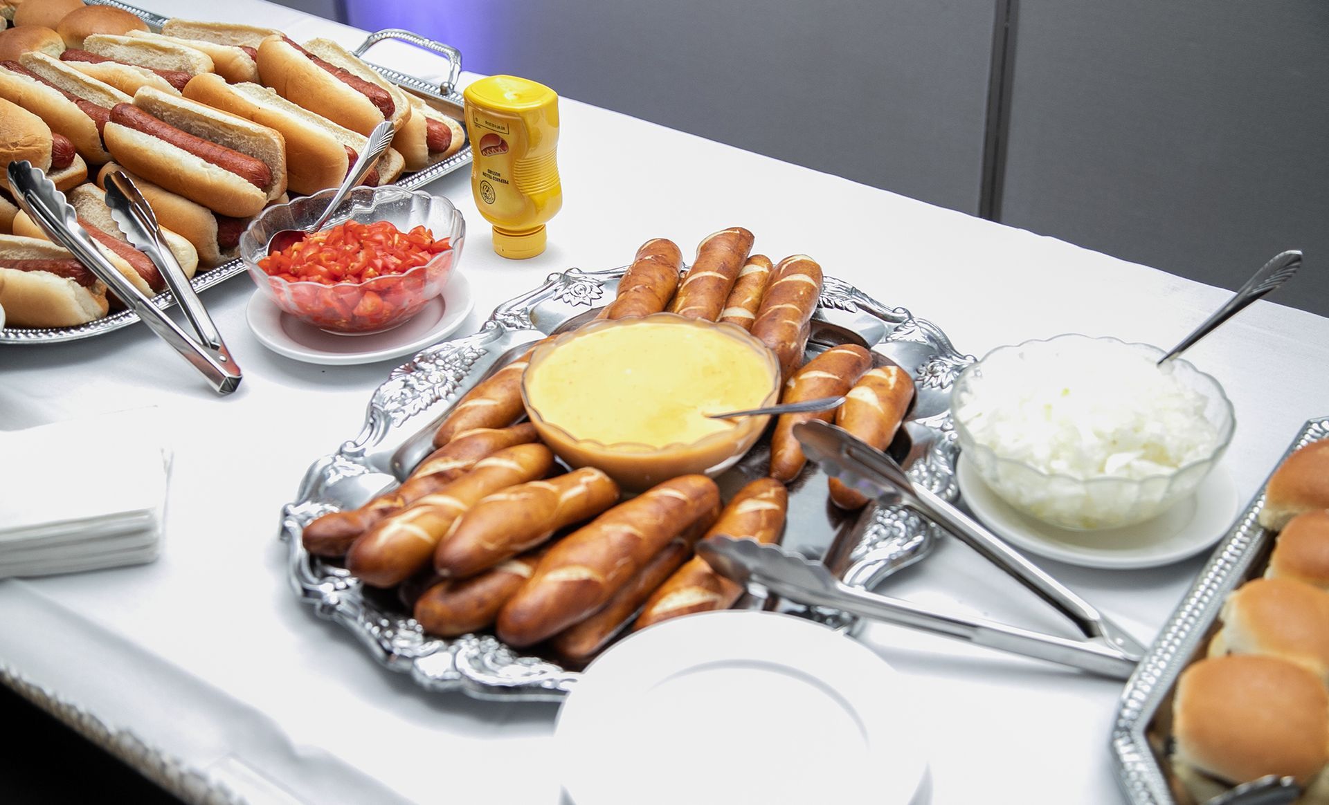 A tray of hot dogs and pretzels on a table with condiments.