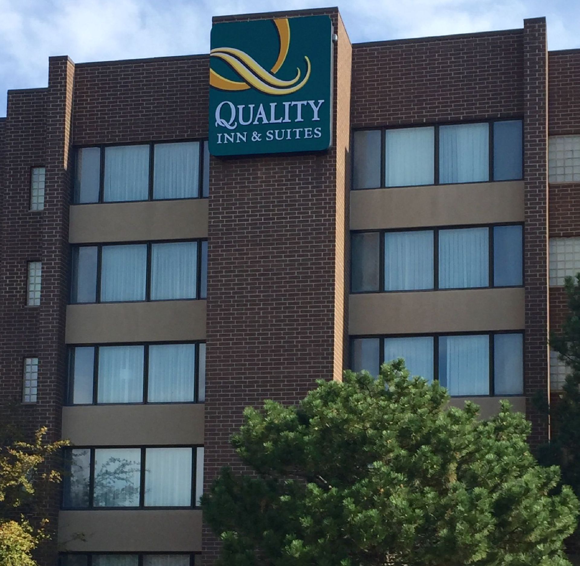 Quality Inn & Suites hotel exterior with a brick facade. Green sign with logo above the entrance.