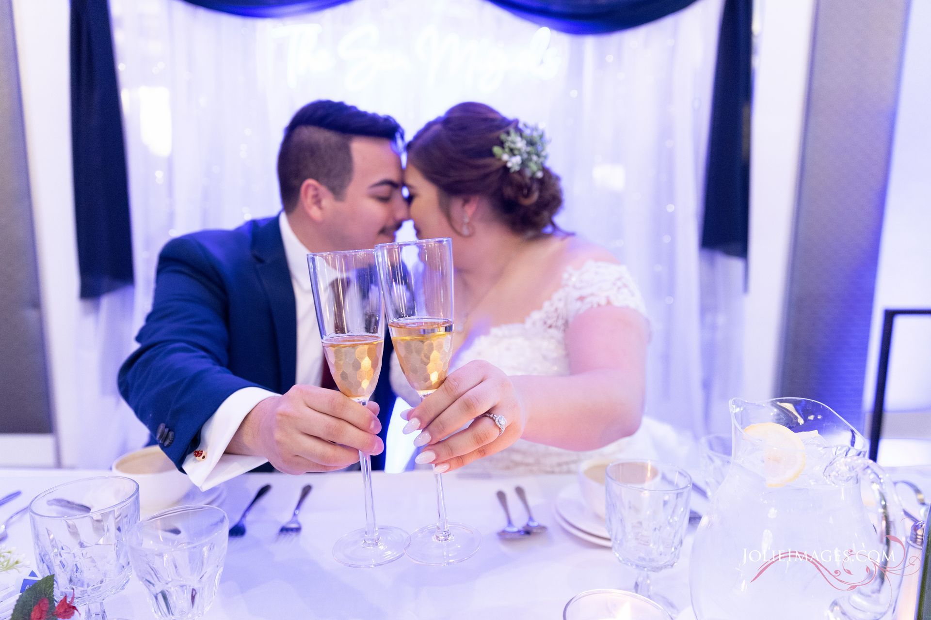 A bride and groom are kissing while toasting with champagne glasses at their wedding reception.