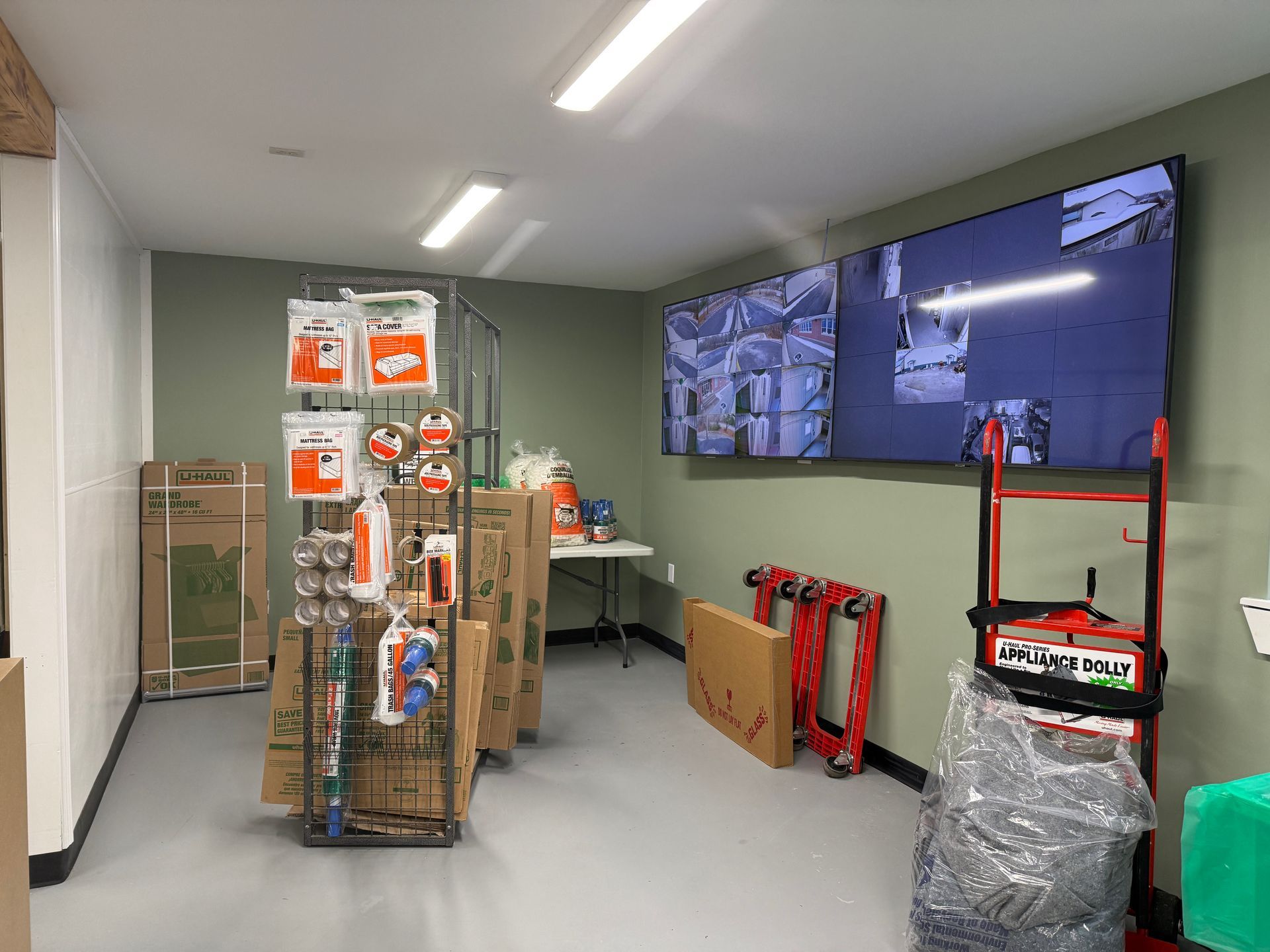 Interior of a storage facility store; shelves of supplies, monitors displaying security footage, and moving equipment.