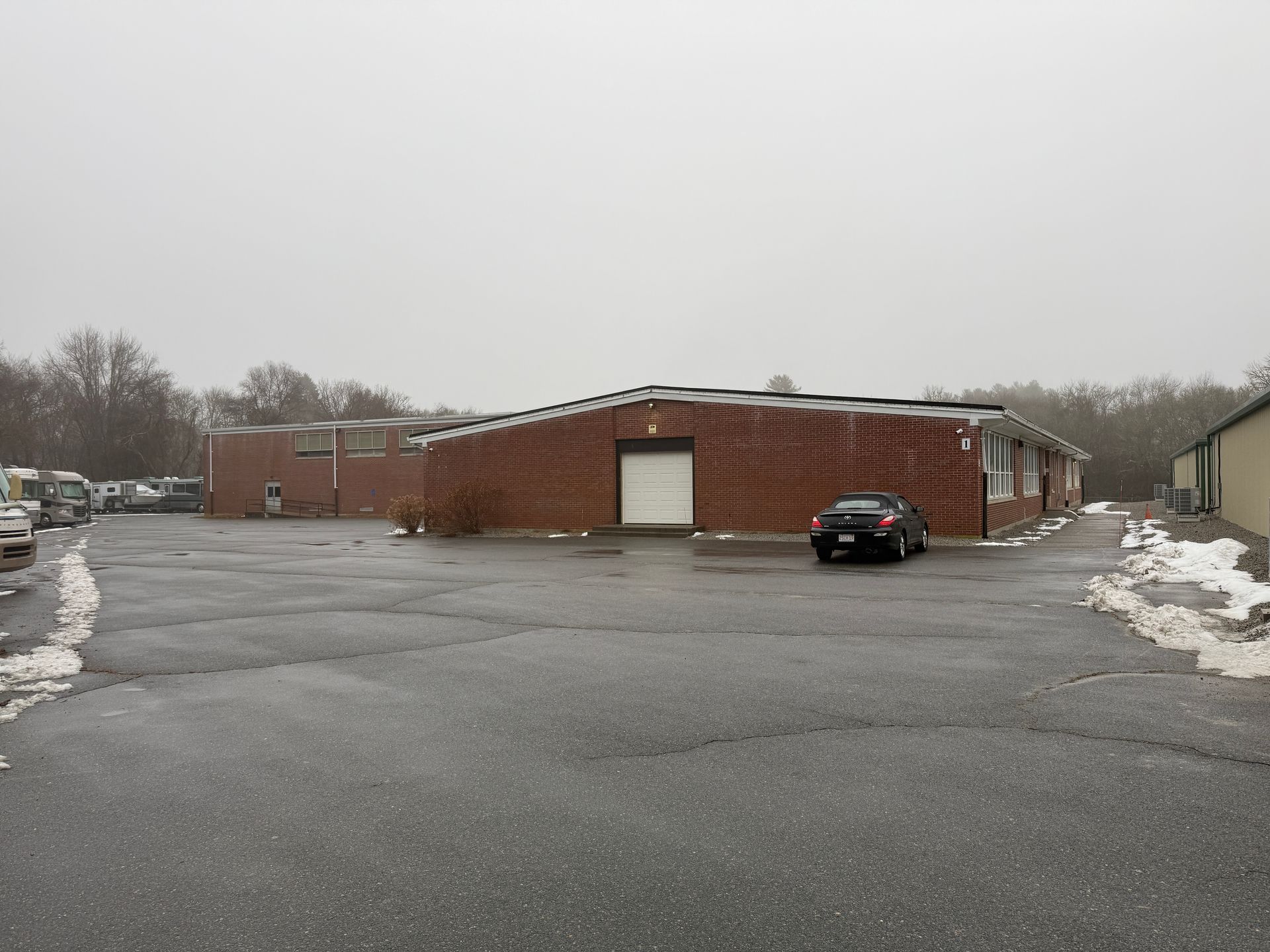 A brick building with a garage door and parked cars on a gray, overcast day.