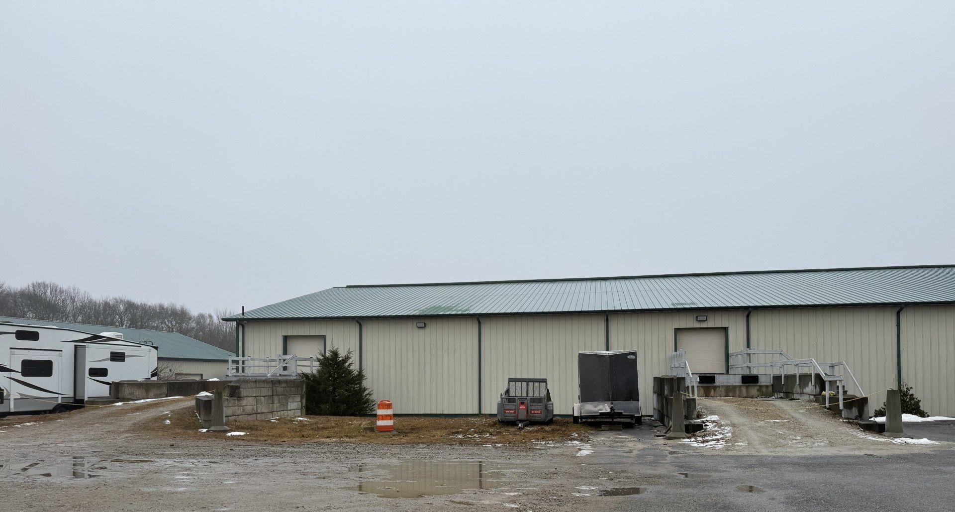 Exterior of a warehouse with loading docks, parked RVs, and a cloudy sky.