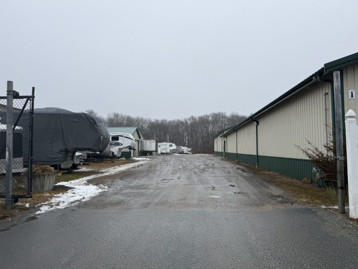 Gravel driveway between a long building and parked vehicles. Overcast day.