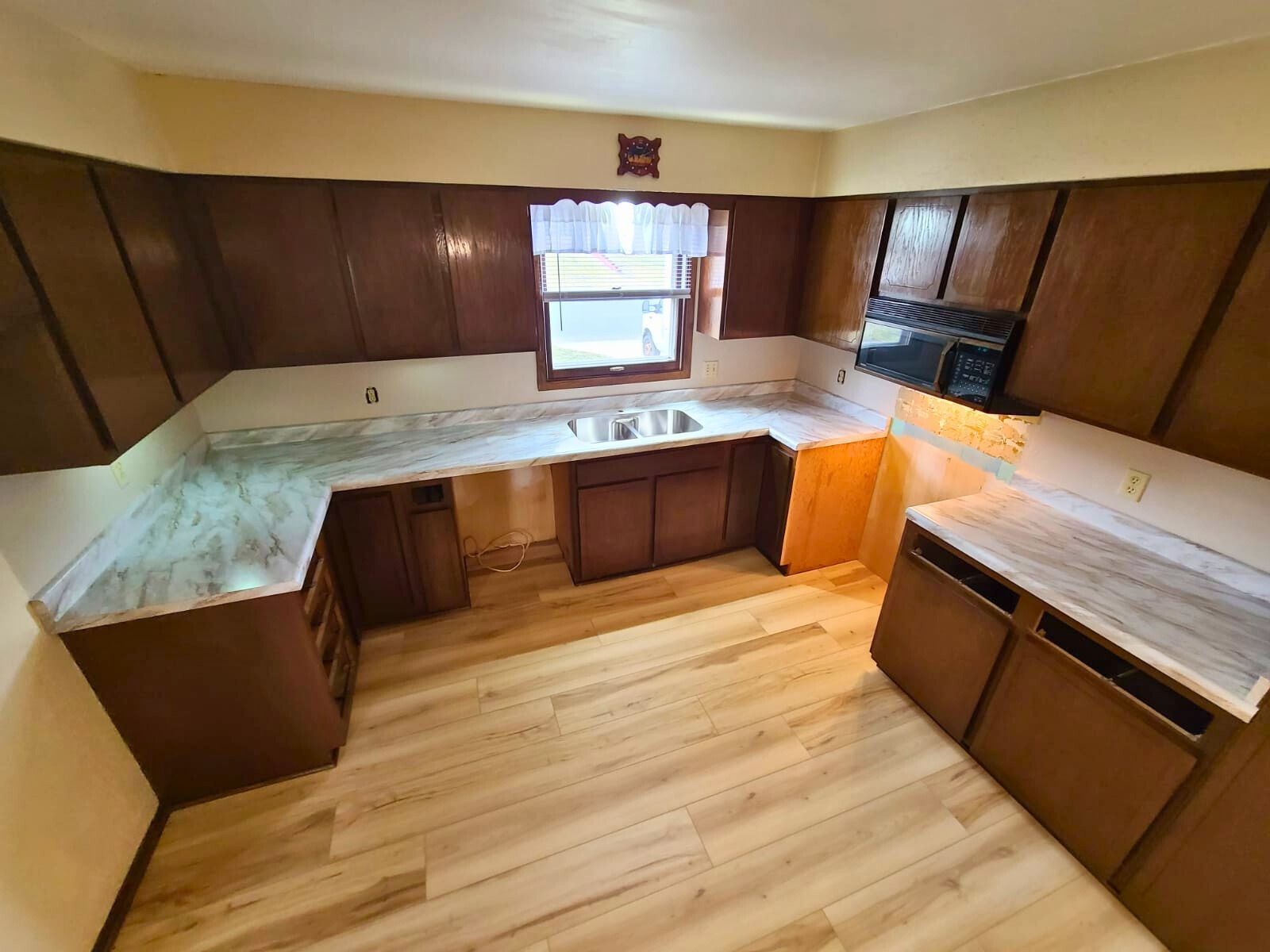 Brown kitchen cabinets with light countertops and flooring. Window above the sink. - after
