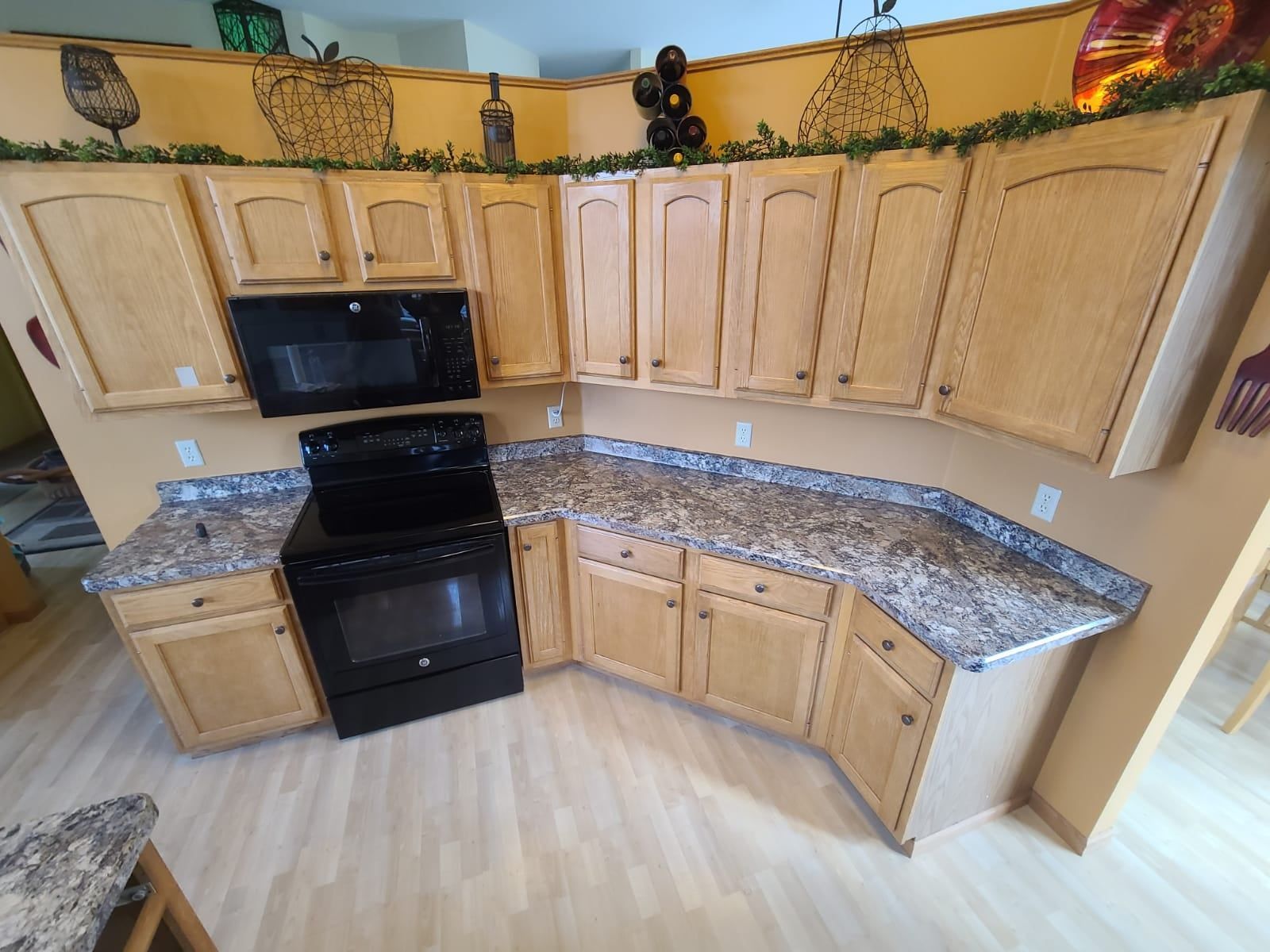 Kitchen with light wood cabinets, black appliances, and speckled countertops. - after