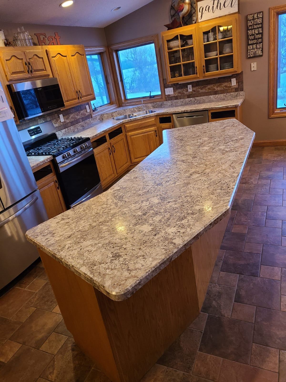 A kitchen with light wood cabinets, gray countertops, and a large island. The floor is tiled. - after