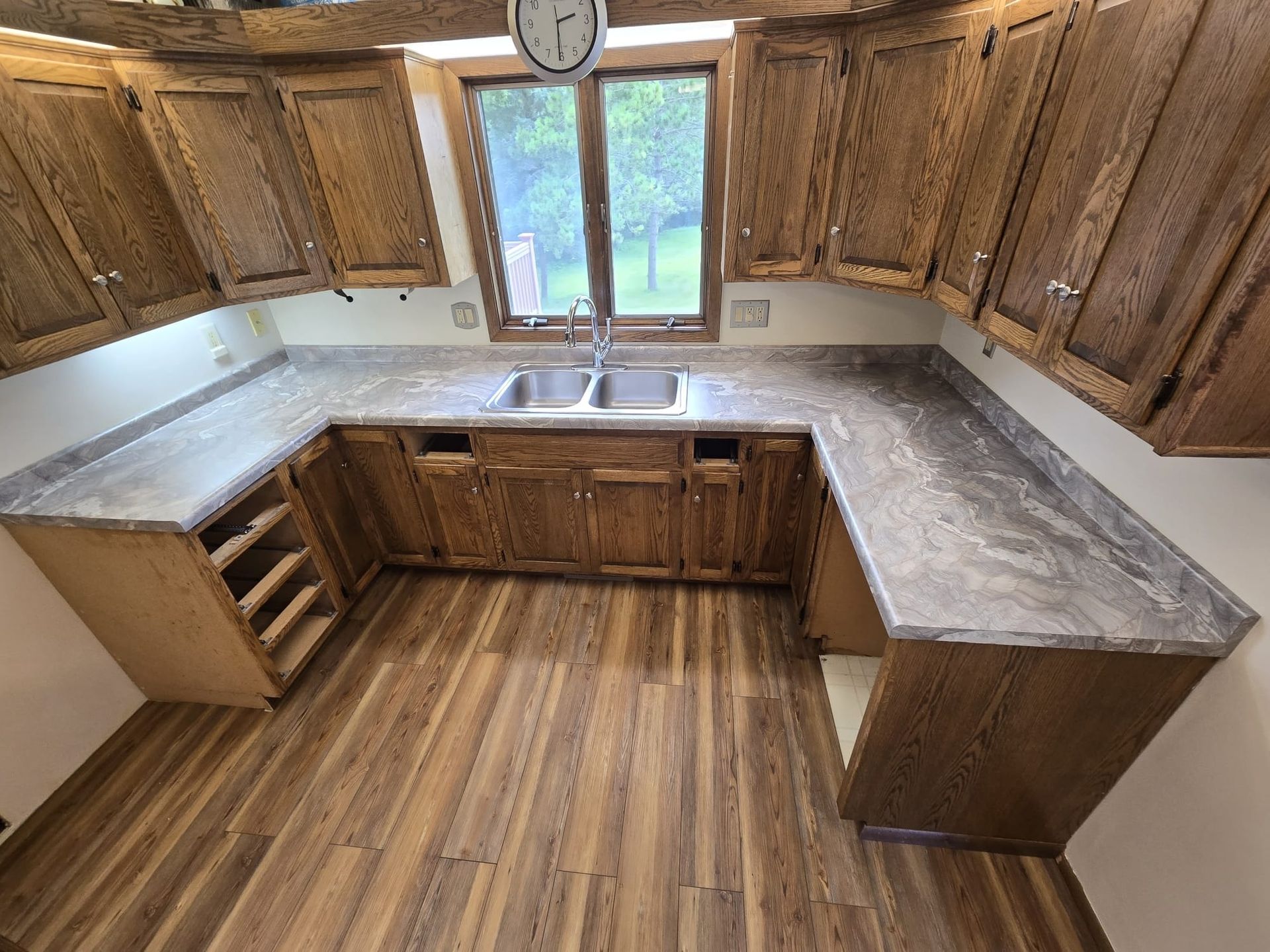 U-shaped kitchen with brown cabinets, gray countertops, and wood-look flooring. - after