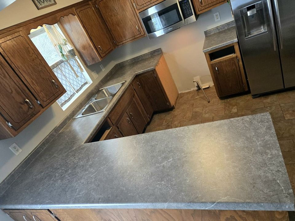 U-shaped kitchen with brown cabinets, gray countertops, stainless steel appliances, and a window. - after