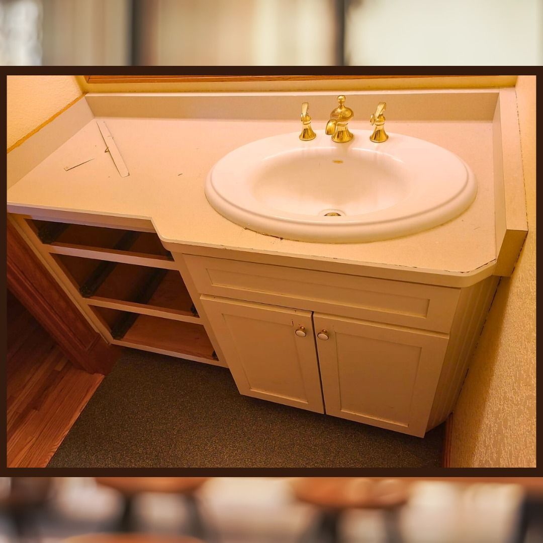 Cream-colored bathroom vanity with a white sink and gold faucet, cabinets, and open shelving. - before