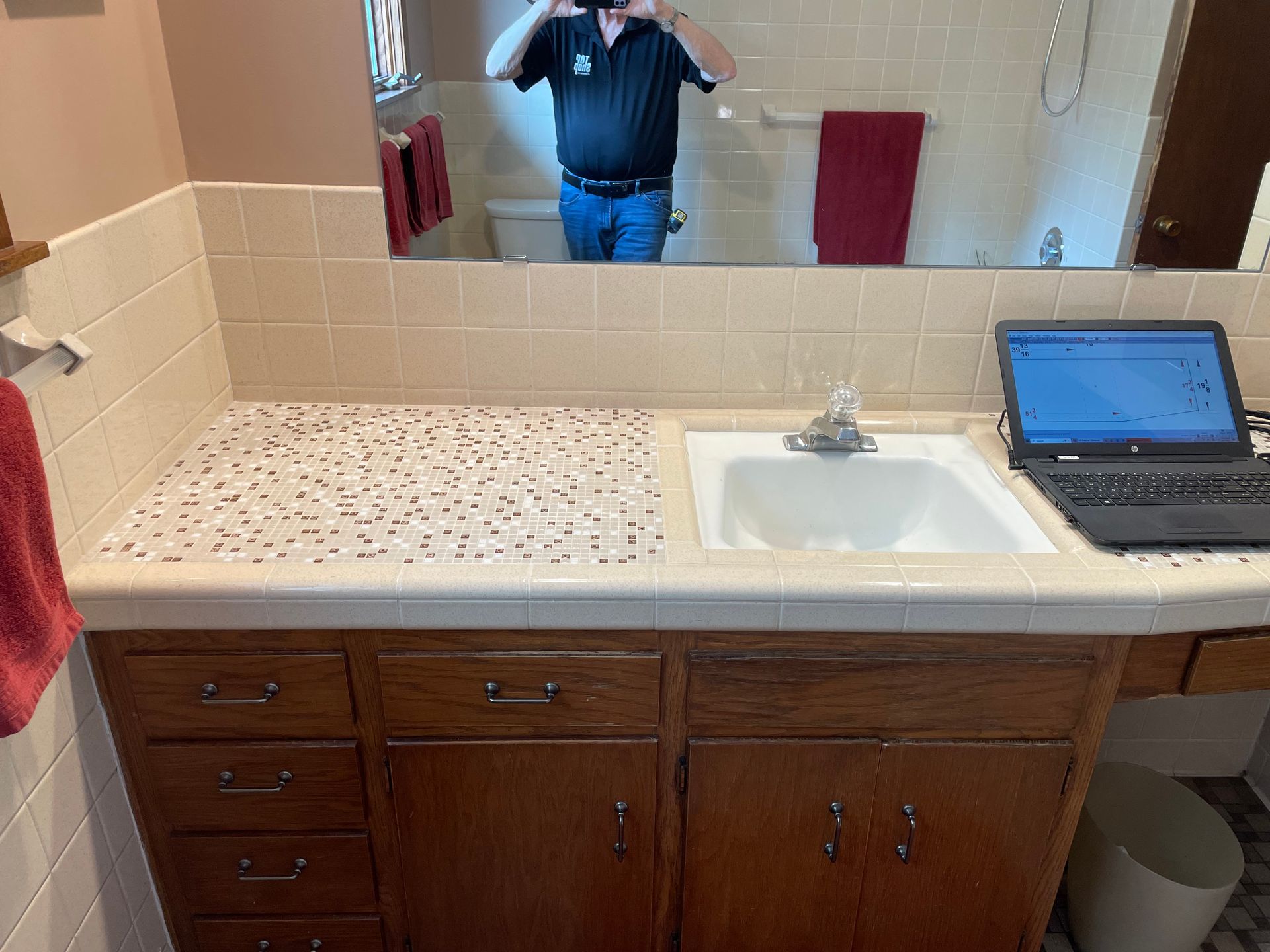 Bathroom vanity with sink, mosaic countertop, wood cabinets, person reflected in mirror. - before