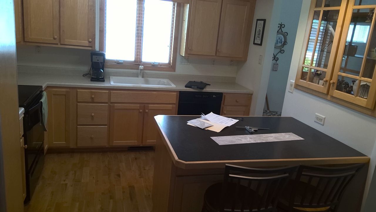 Kitchen with wooden cabinets, a sink, and a black countertop island with two chairs.