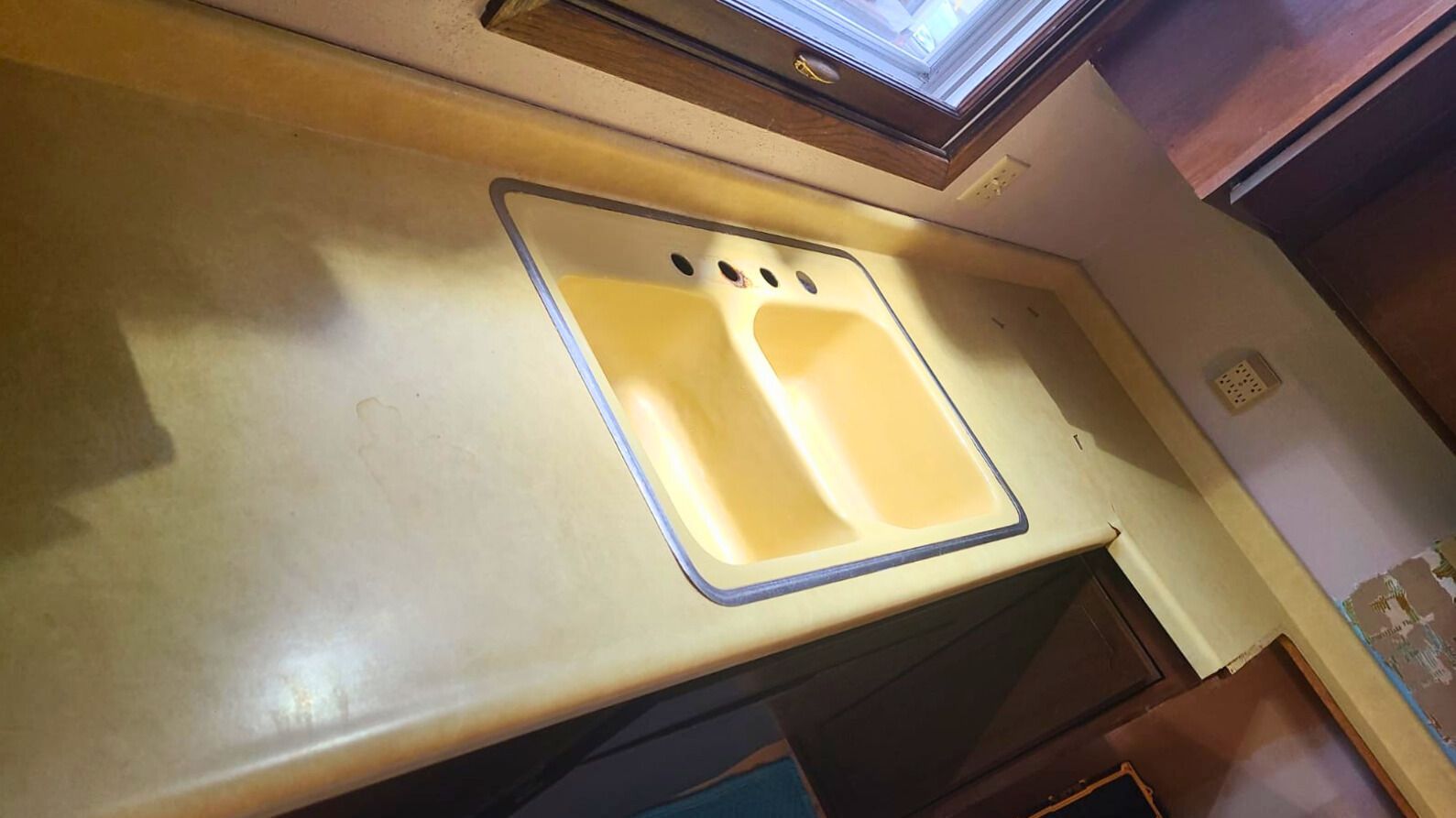 A light yellow sink with two basins set in a matching countertop, inside a boat. - before
