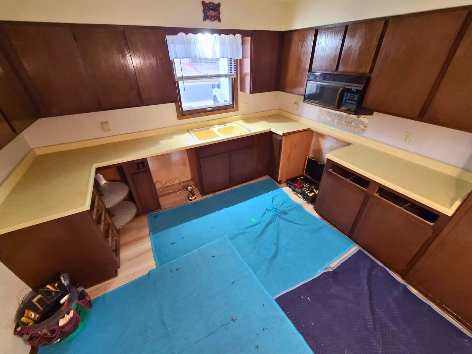 Kitchen renovation in progress: dark wood cabinets, yellow countertops, tools and blue pads on the floor. - before