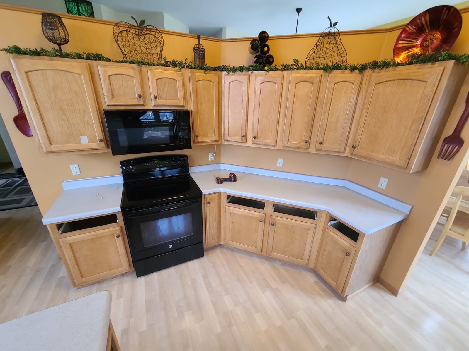 Kitchen with light wood cabinets, black appliances, and white countertops. - before