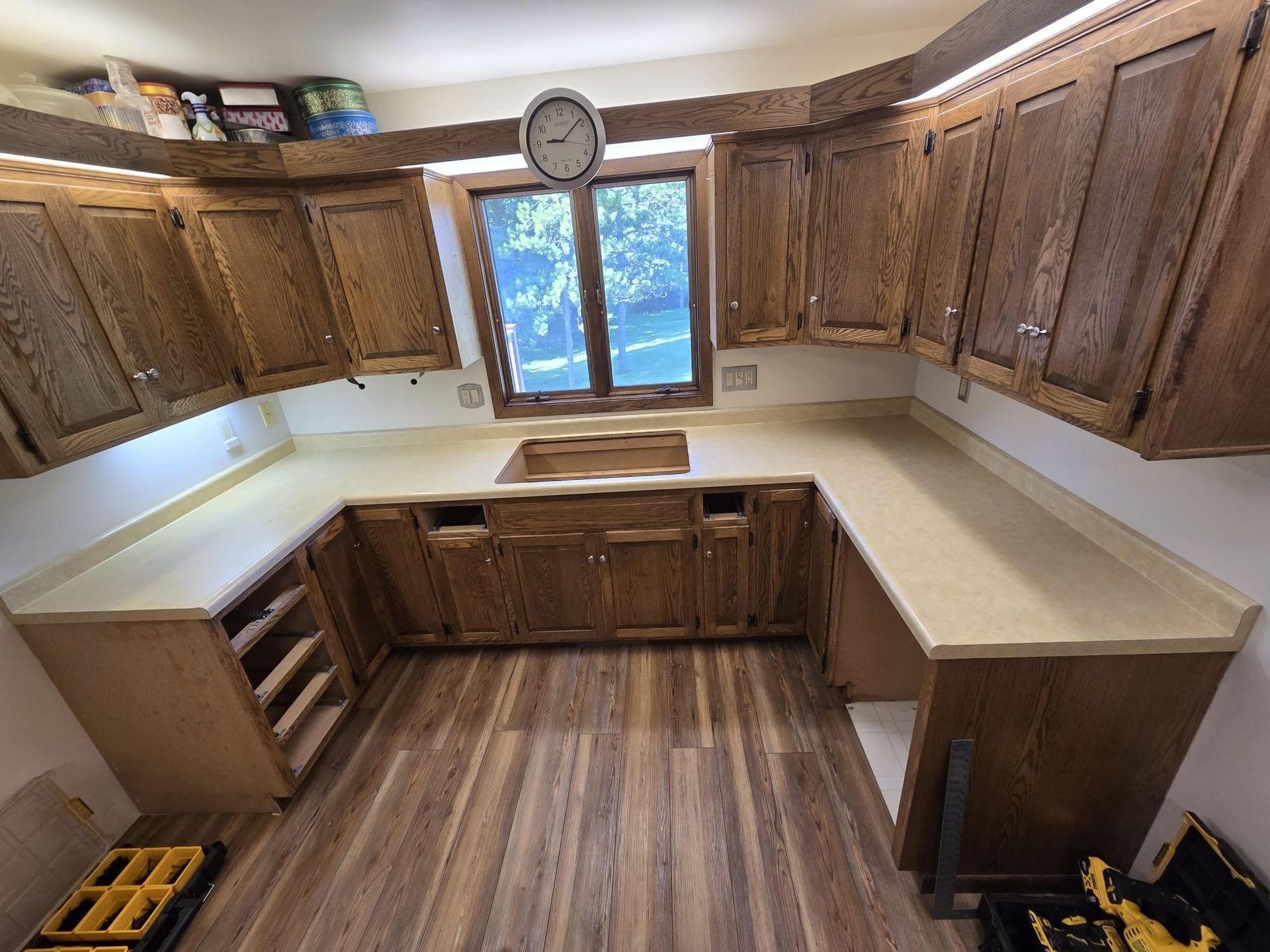 U-shaped kitchen with wood cabinets, light countertops, and a window. Wood-look flooring. - before