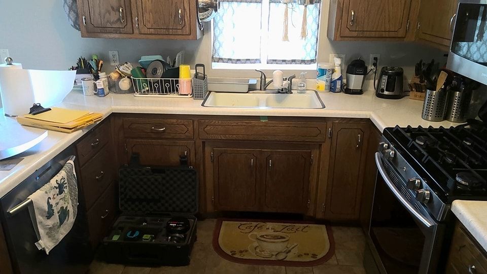 Kitchen with brown cabinets, sink, and stove. Dishes and utensils are visible. - before