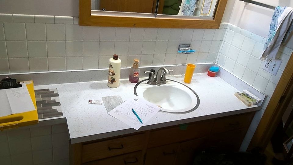 Bathroom vanity with a sink, mirror, and toiletries. Construction in progress: tile and documents on the countertop. - before