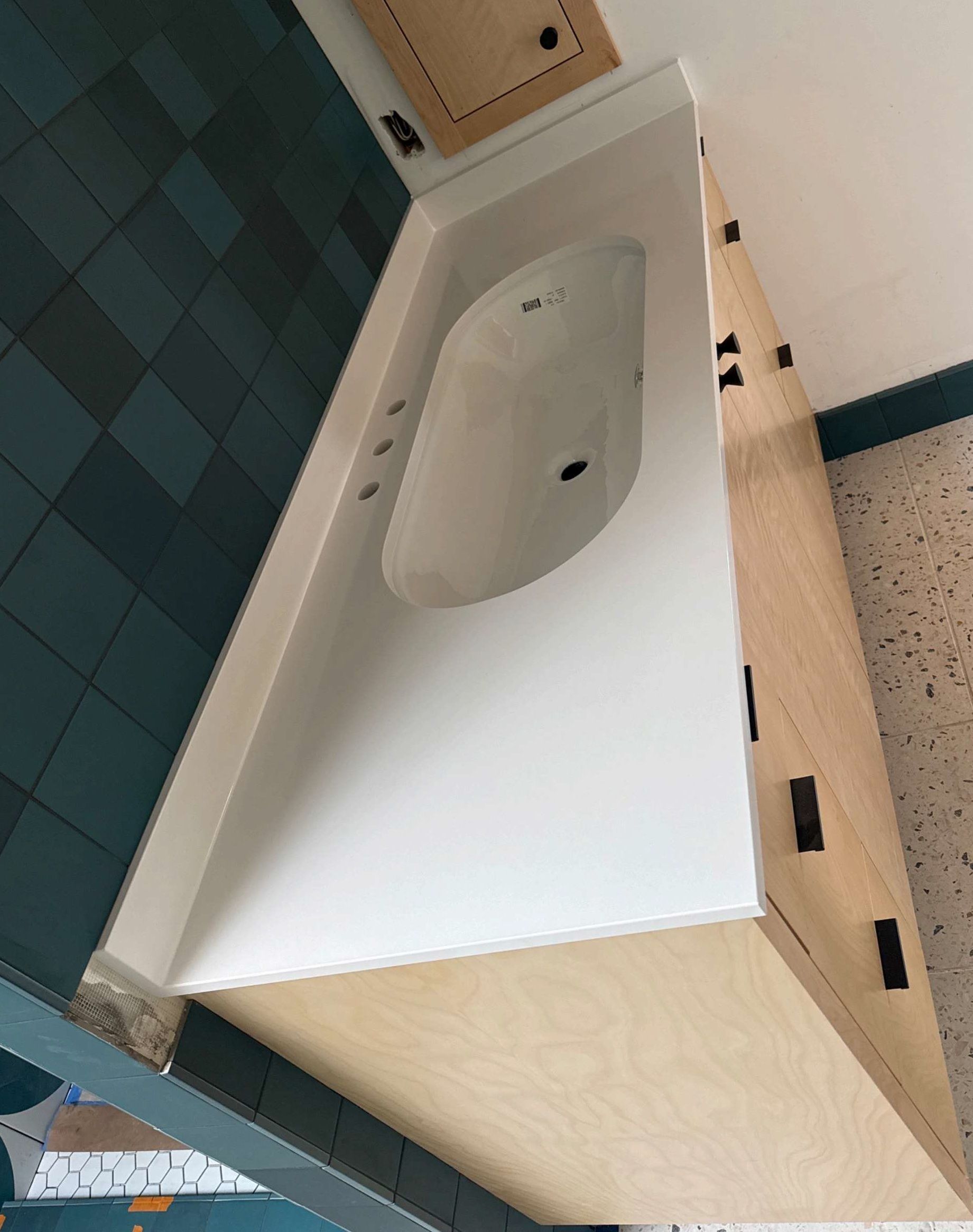 Bathroom sink vanity with white countertop, oval basin, and teal tiled wall