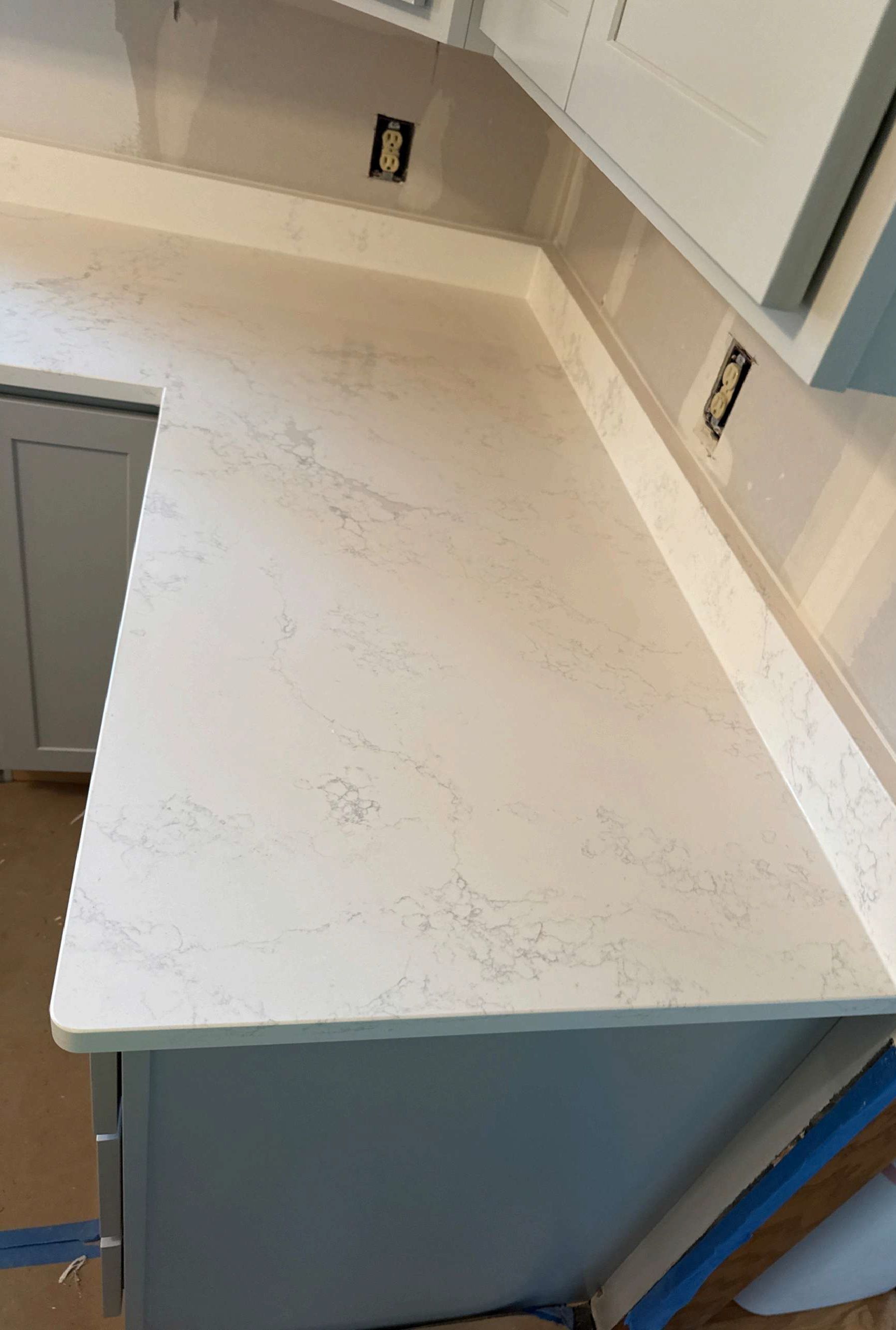 White quartz countertop under construction with gray cabinet fronts and unfinished backsplash area