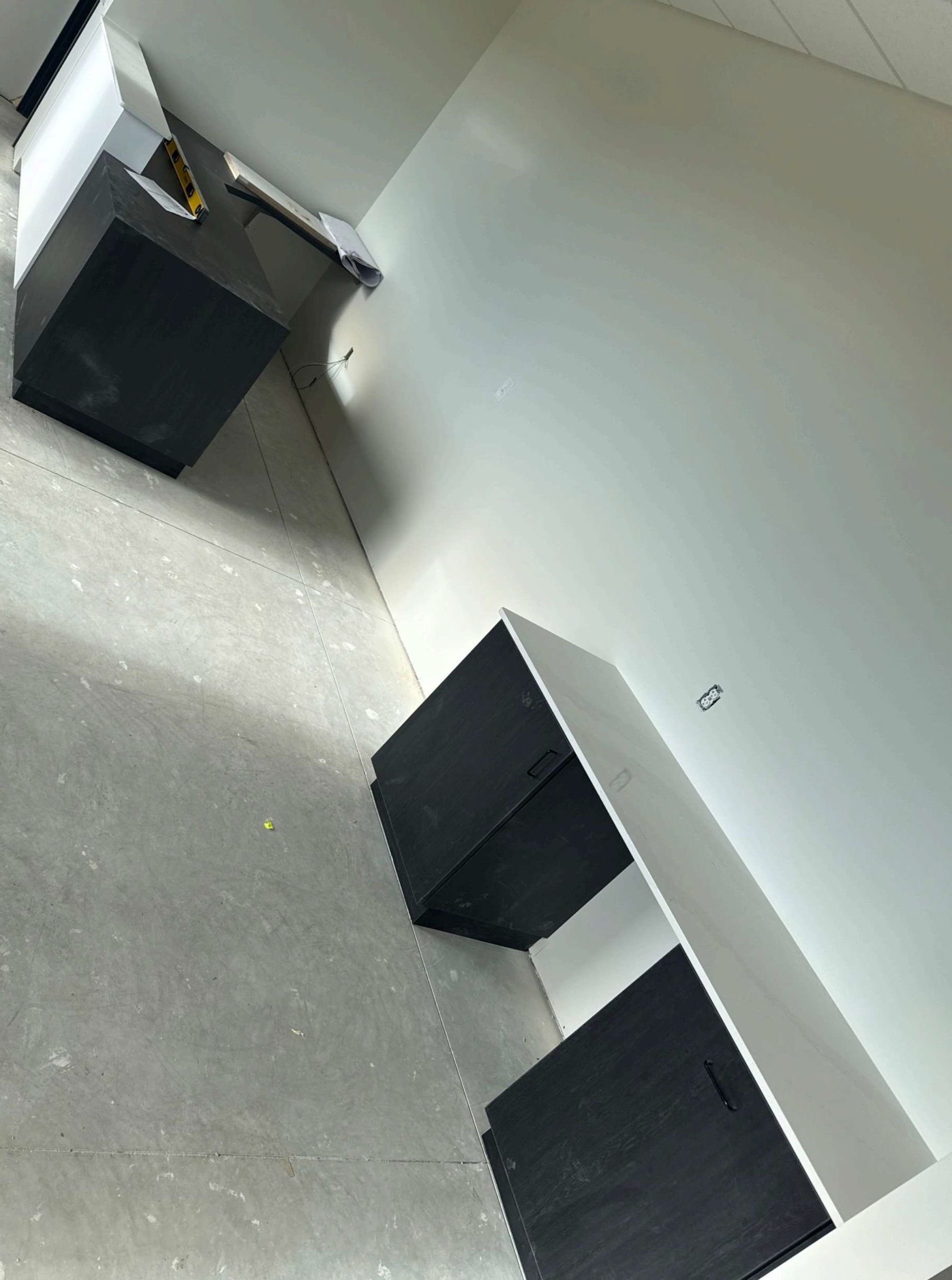 Empty office room with white walls, gray carpet, and two black cabinets against the walls.