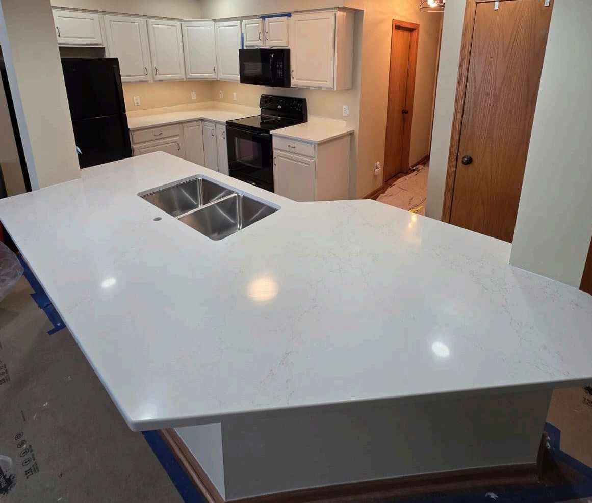Modern kitchen with white island countertop and built-in sink, cabinets, stove, and refrigerator in the background