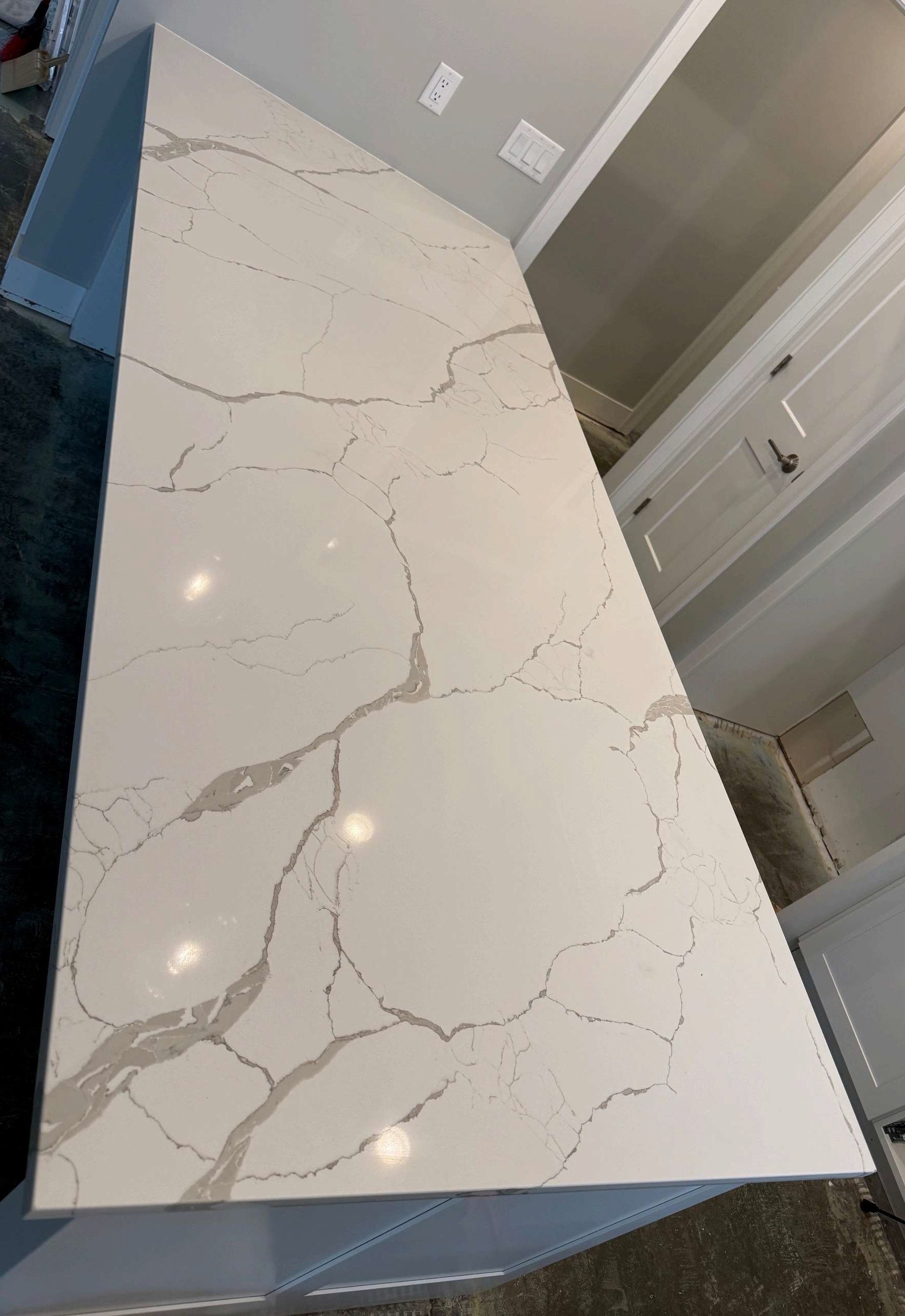 White marble-look kitchen island countertop with gray veining and lights reflected on its glossy surface