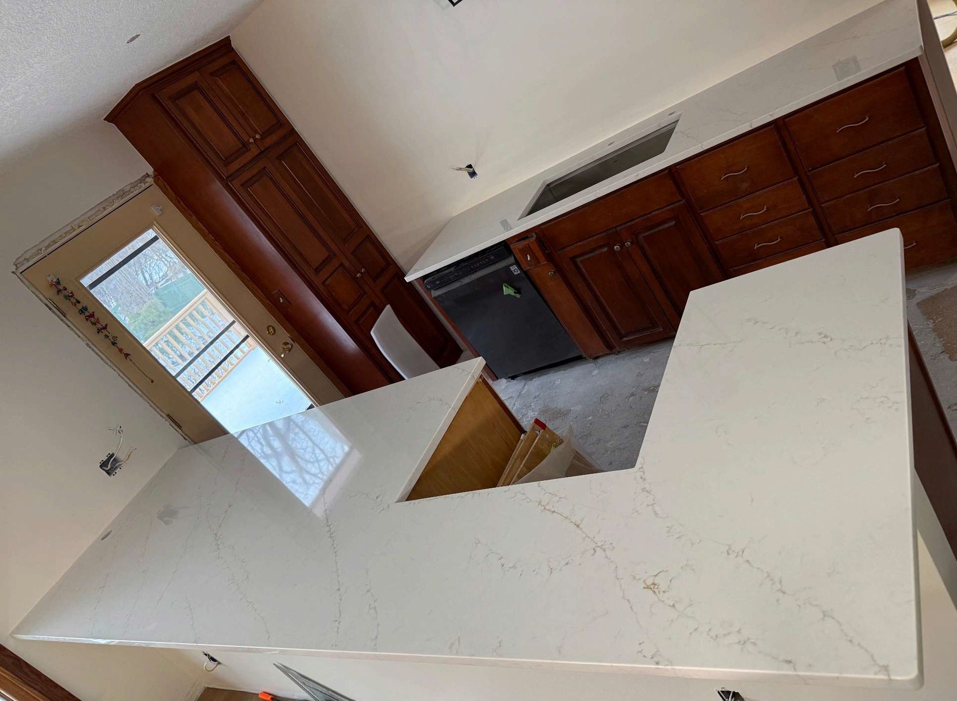 Empty kitchen with white island countertop, dark wood cabinets, and a tiled floor.